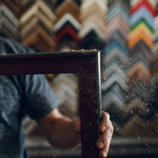 Framing Workshop. Master blows off dust baguette handmade picture frame at studio.